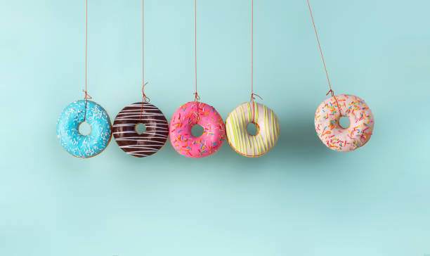Collision balls made from donuts Newton's cradle from doughnuts. Collision balls made from donuts. Harm of sugar, donuts time or healthy diet concept. Dependence on flavoring, diabetes problems, weight loss. balance photos stock pictures, royalty-free photos & images