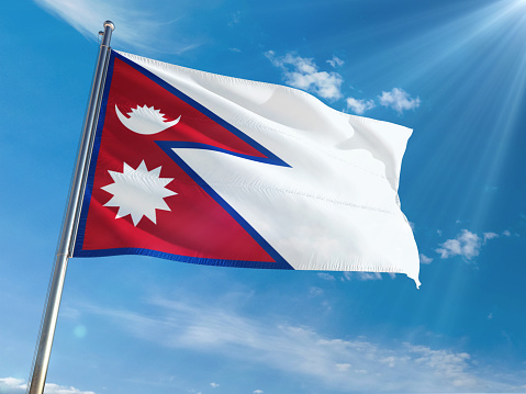 Nepal National Flag Waving on pole against sunny blue sky background. High Definition
