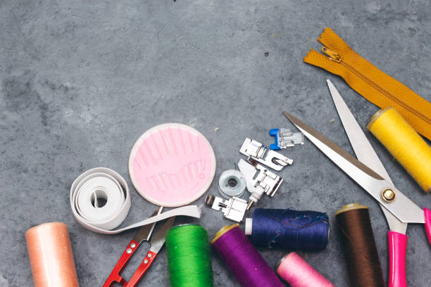 istock sewing tools :  scissors, colorful  bobbins with thread and presser foot on gray  wooden table, top view - Image 1128979561