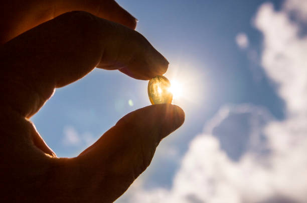 Vitamin D keeps you healthy while lack of sun. Yellow soft shell D-vitamin capsule against sun and blue sky on sunny day. Cure concept. stock photo