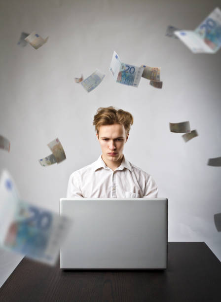 istock Young man using a laptop to browse the net. Young worker and falling Euro banknotes. Currency and job concept. 1128987377
