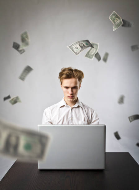 istock Young man using a laptop to browse the net. Young worker and falling dollar banknotes. Currency and job concept. 1128987378