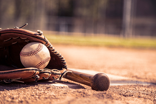 Spring and summer baseball season is here.  Wooden bat, glove, and weathered ball lying on home plate in late afternoon sun.   No people.  Great background image.