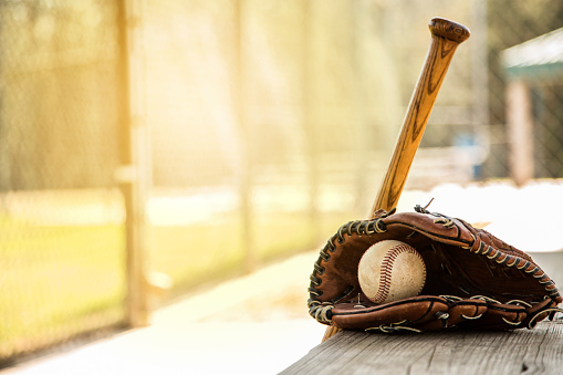 Spring and summer baseball season is here.  Wooden bat, glove, and weathered ball lying on dugout bench in late afternoon sun.  No people.  Great background image.