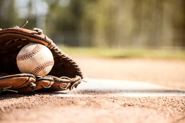 Baseball season is here.  Glove and ball on home plate. Spring and summer baseball season is here.  Wooden bat, glove, and weathered ball lying on home plate in late afternoon sun.  Dugout in background.  No people.  Great background image. baseball baseballs spring training professional sport stock pictures, royalty-free photos & images