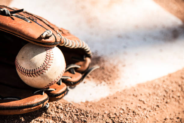 Baseball season is here.  Glove and ball on home plate. Spring and summer baseball season is here.  Wooden bat, glove, and weathered ball lying on home plate in late afternoon sun.  Dugout in background.  No people.  Great background image. baseball baseballs spring training professional sport stock pictures, royalty-free photos & images