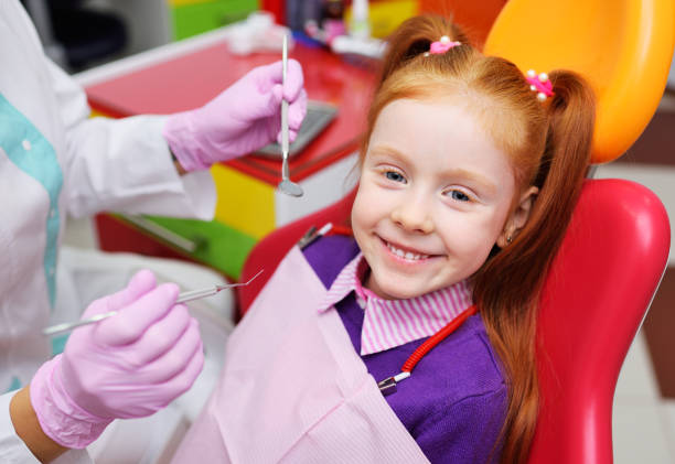 the child is a little red-haired girl smiling sitting in a dental chair. stock photo