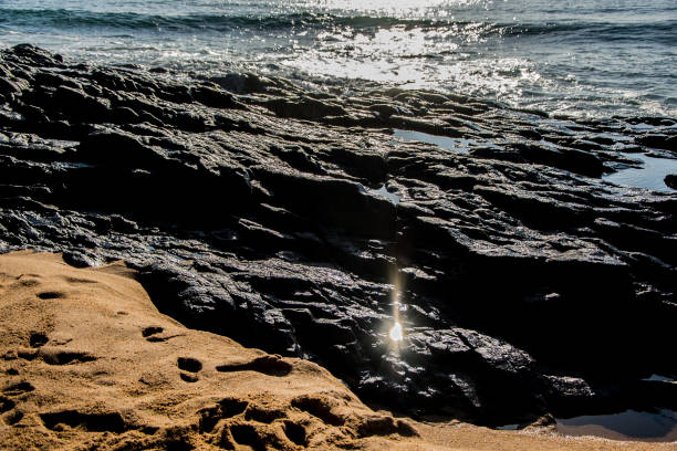 Shots of the variety of colors in waves as they hit the sand, moving to cover and flow into volcanic stone on the beach.