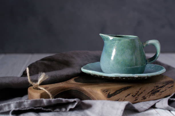 istock Natural handcrafted dishware. Wooden brown cutting board and ceramic blue cream jug with gray linen napkin. Country, rustic style 1128997672