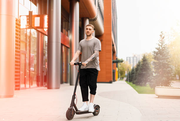 istock Attractive young man riding a kick scooter at cityscape background. 1128997680