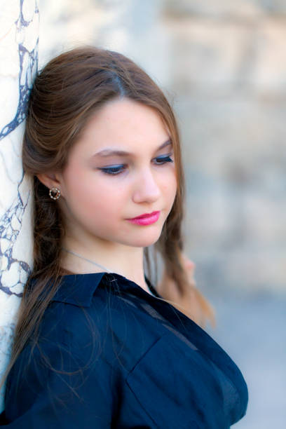 A portrait shot captures a beautiful young woman with long, flowing brown hair and striking brown eyes looking directly at the camera with a slightly pensive expression. She is wearing a white top with delicate lace details.