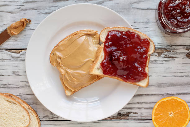 Open face homemade peanut butter and strawberry Jelly sandwich Top view of open face homemade peanut butter and strawberry Jelly sandwich on oat bread, over a white rustic wooden table / background. Served with fresh oranges / fruit. peanut butter and jelly sandwich stock pictures, royalty-free photos & images