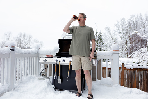 Hombre maduro a la parrilla mientras bebe cerveza durante la temporada de invierno photo
