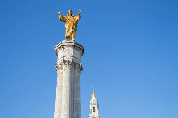 Golden Christ Statue 100th Cellebration Mary's Appearance Basilica of Lady of Rosary Bell Tower Fatima Portugal. Church created on site where three Portuguese Shepherd children saw Virgin Mary of the Rosary.  Basilica created in 1953. Banners are based on old pictures of two peasant children