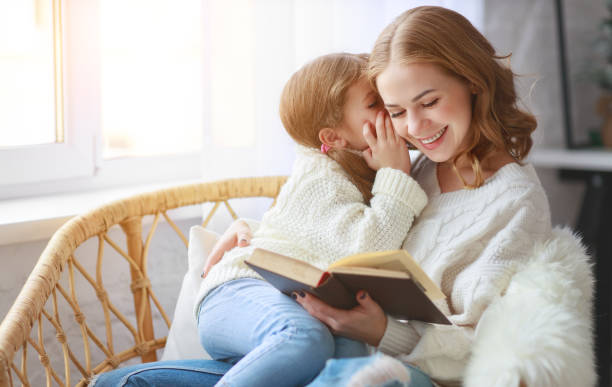 счастливая мать семьи читает книгу ребенку к дочери у окна - family with one child domestic life caucasian love стоковые фото и изображения