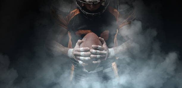 American football player on a dark background in smoke in black and orange equipment. American football player on a dark background in smoke in black and orange equipment. american football ball photos stock pictures, royalty-free photos & images