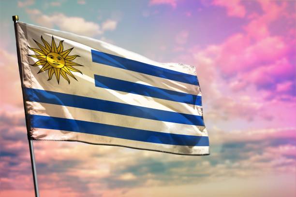 istock Fluttering Uruguay flag on colorful cloudy sky background. Prosperity concept. 1129016313