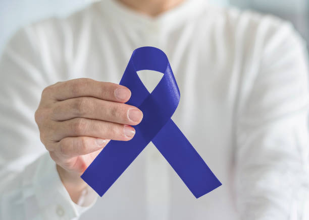 cinta del conocimiento del cáncer colorrectal colon concepto salud de los hombres con el arco azul del color en la mano de la persona - acomodador fotografías e imágenes de stock