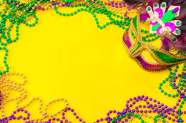 Fat Tuesday and Mardi Gras carnival concept theme with close up on a face mask full of color, feathers and texture and golden, green and purple beads isolated on yellow background with copy space Fat Tuesday and Mardi Gras carnival concept theme with close up on a face mask full of color, feathers and texture and golden, green and purple beads isolated on yellow background with copy space new orleans mardi gras stock pictures, royalty-free photos & images