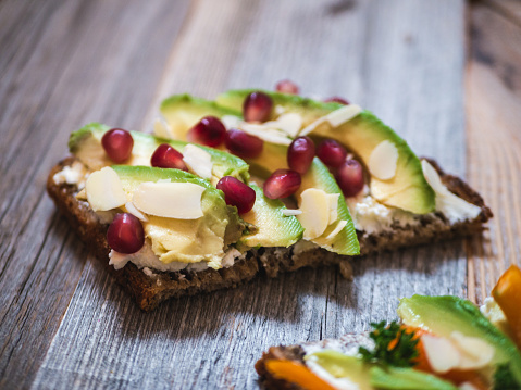 Delicious and healthy avocado toast with pomegranate, bell pepper and almond on rustic wooden board