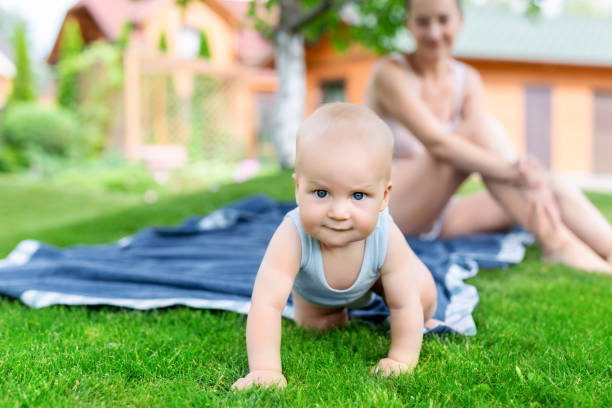 かわいいの白人の男の子が母親と一緒に庭で楽しんでの肖像画。庭で母と散歩中に緑の草の芝生の上でクロールの子。幸せな子供時代と赤ちゃんのヘルスケア - fun walk ストックフォトと画像