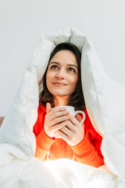 Young woman having coffee under the duvet