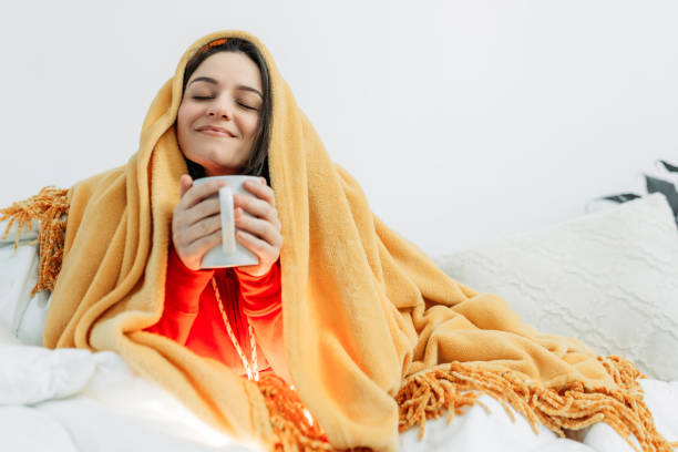 Young woman having coffee under the duvet