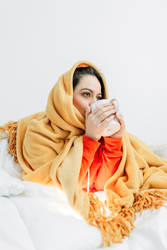 Young woman having coffee under the duvet