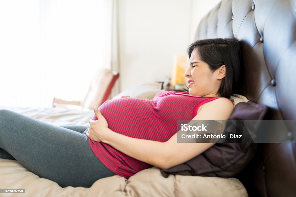 Woman Suffering From Braxton Hicks Contractions Side view of stressed woman getting regular contractions on bed Muscular Contraction Stock Photo