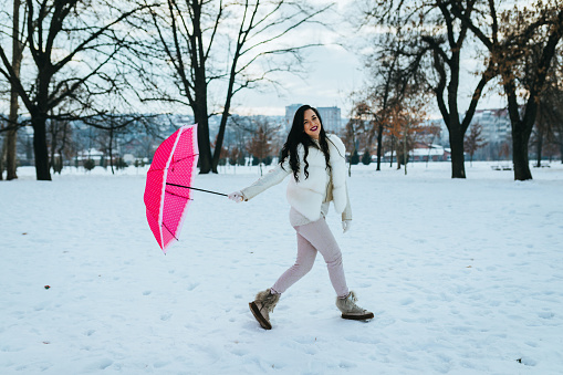 Cheerful woman with a pink umbrella enjoying snowy winter day