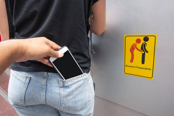 Thief stealing mobile phone from back pocket of a woman with beware pickpockets sign symbol background Thief stealing mobile phone from back pocket of a woman with beware pickpockets sign symbol background pickpocketing stock pictures, royalty-free photos & images