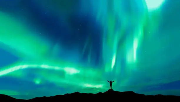 Photo of Aurora borealis with silhouette standing man on the mountain.Freedom traveller journey concept