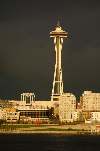 Seattle, Washington, USA, waterfront in impending thunderstorm. Olympic Sculpture Park in foreground with red Eagle sculpture, taller buildngs of Seattle Center including arches of Pacific Science Center and the Space Needle in back.