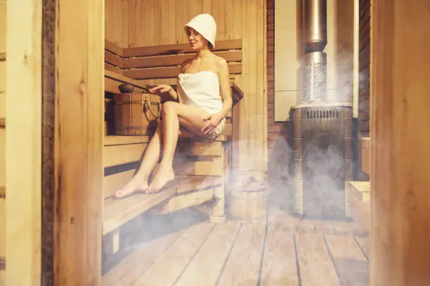 Photo of Young beautiful woman relaxing in the Finnish sauna wrapped. Interior of Finnish sauna, classic wooden sauna, Relax in hot sauna