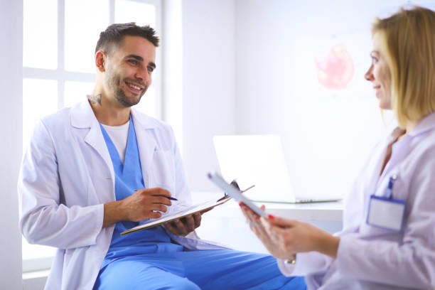 istock Handsome doctor is talking with young female patient and making notes while sitting in his office 1129068069