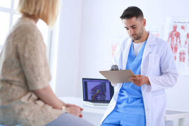 istock Handsome doctor is talking with young female patient and making notes while sitting in his office 1129069474