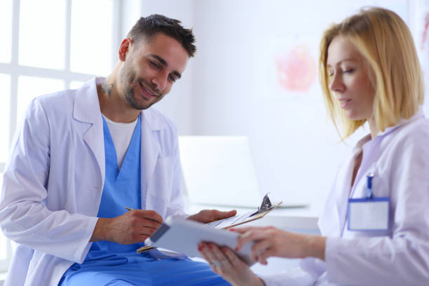 istock Handsome doctor is talking with young female patient and making notes while sitting in his office 1129069522