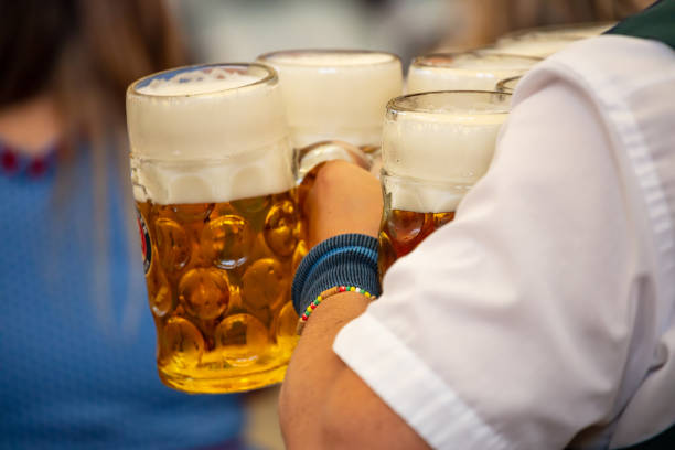 Beer Fest celebration. Waiter is serving huge glasses with beer with foam. Blur background, closeup view. Beer Fest celebration. Waiter is serving huge glasses with beer, wearing a traditional costume. Blur background, closeup view. large german beer steins stock pictures, royalty-free photos & images