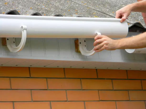 Contractor installing plastic roof gutter. Plastic Guttering  Replace, Rain Guttering & Drainage Repair by Handyman hands.