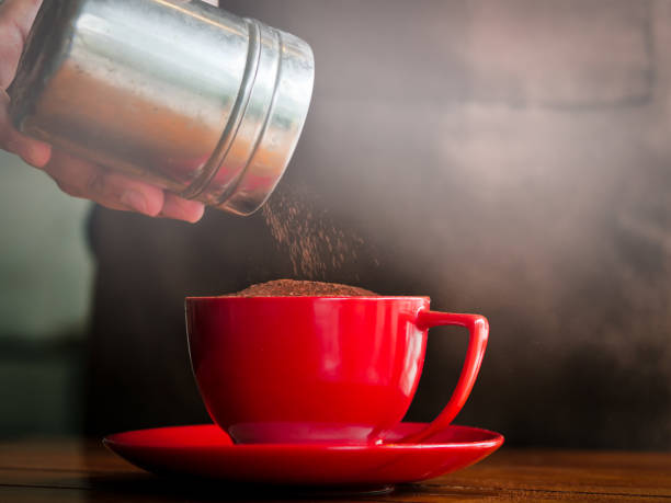 istock Hand sprinkles chocolate powder on red coffee mug. 1129075419