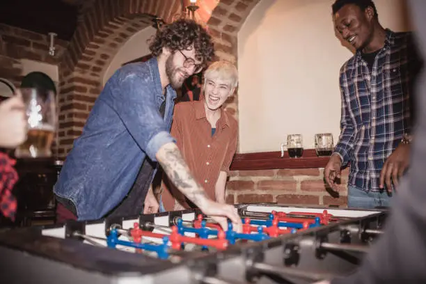 Group of friends enjoying their time, while playing Foosball in the pub