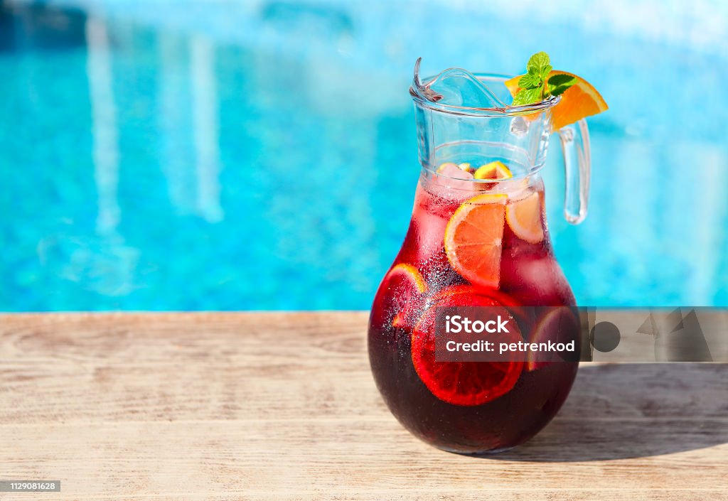 Glass jug of iced sangria with strawberry, orange, apple and lemon Glass jug of iced sangria with strawberry, orange, apple and lemon by the pool Sangria Stock Photo