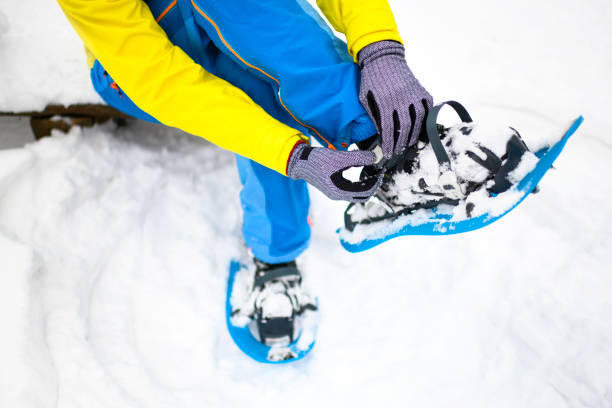 Hiker adjusting her snowshoe straps while sitting on a bench covered with snow.
