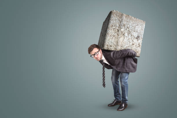 istock Businessman carrying a large and heavy stone on his back 1129083759