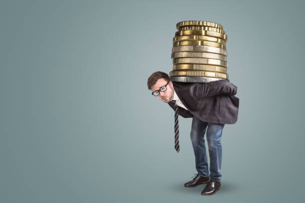 businessman carrying a giant stack of coins on his back - overstrained imagens e fotografias de stock