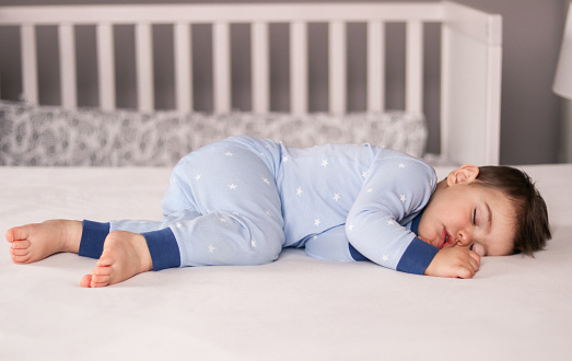 Ð¡ute little baby boy in light blue pajamas sleeping peacefully on bed at home. Child daytime sleeping schedule