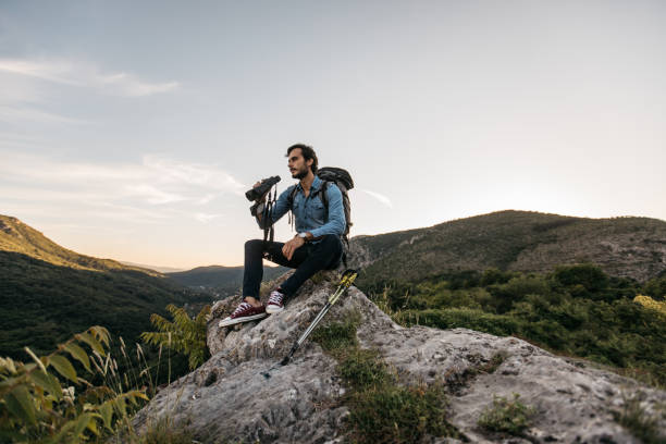 istock Man hiker sitting on mountain rock looking through binoculars 1129090082