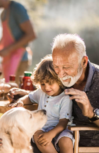 Senior grandparent and his grandkid having fun with a dog in the backyard. Mature man and his small grandchild enjoying on a picnic lunch with their dog. pet owner photos stock pictures, royalty-free photos & images