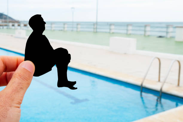 closeup of the hand of a man with a black paper cutout in the shape of a man throwing himself into a swimming pool