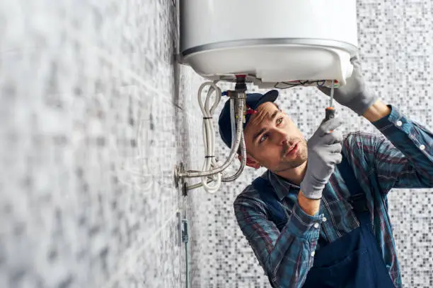 Photo of Almost done. Worker set up electric heating boiler at home bathroom